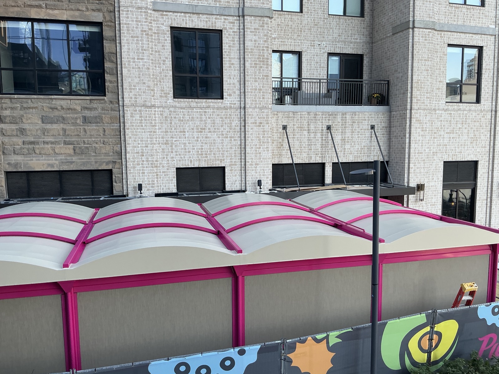 Commercial canopy with a magenta powder-coated frame and arched fabric panels outside a brick building