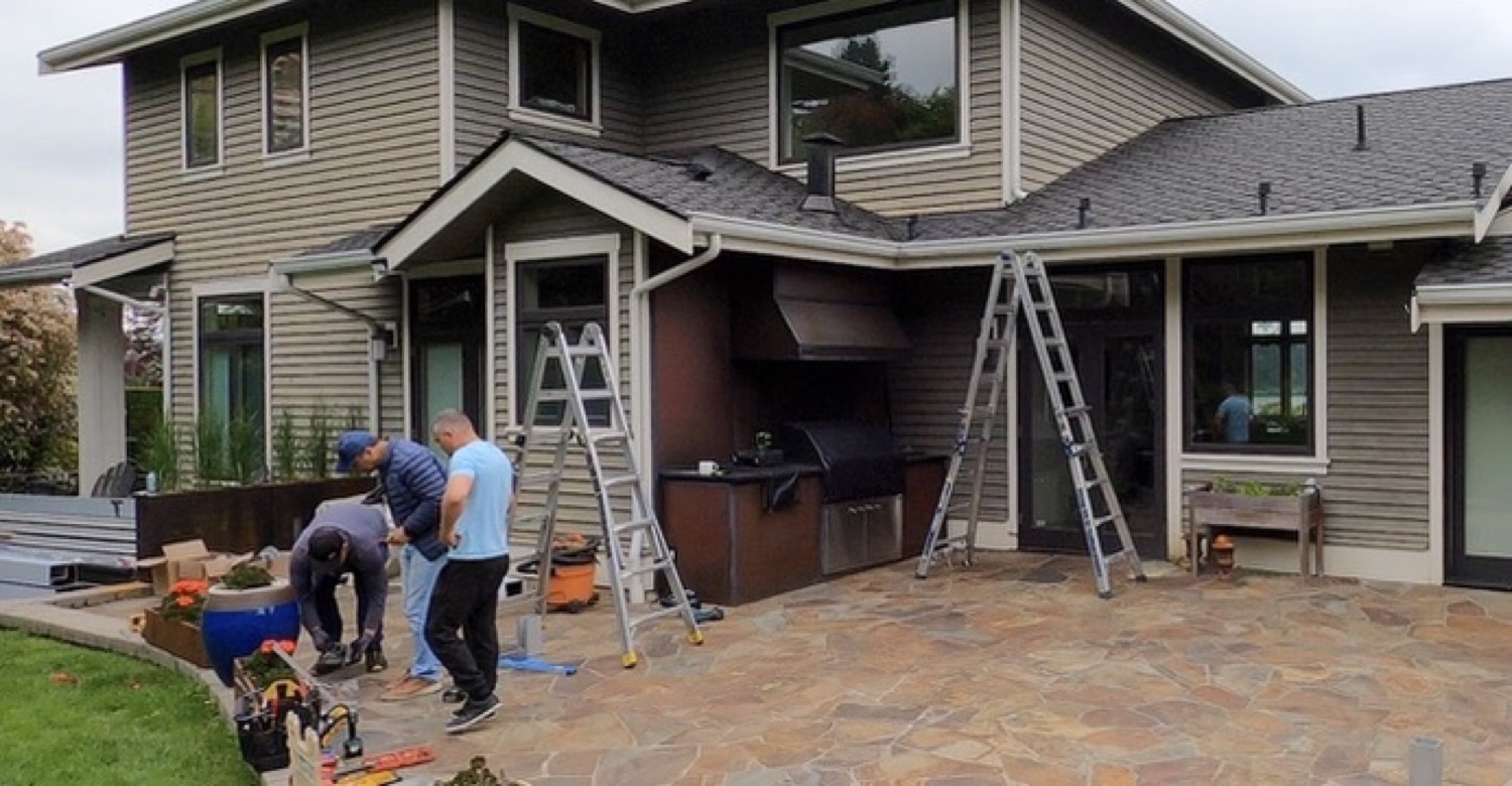 Templar installers on ladders fitting motorized screens around a covered outdoor kitchen