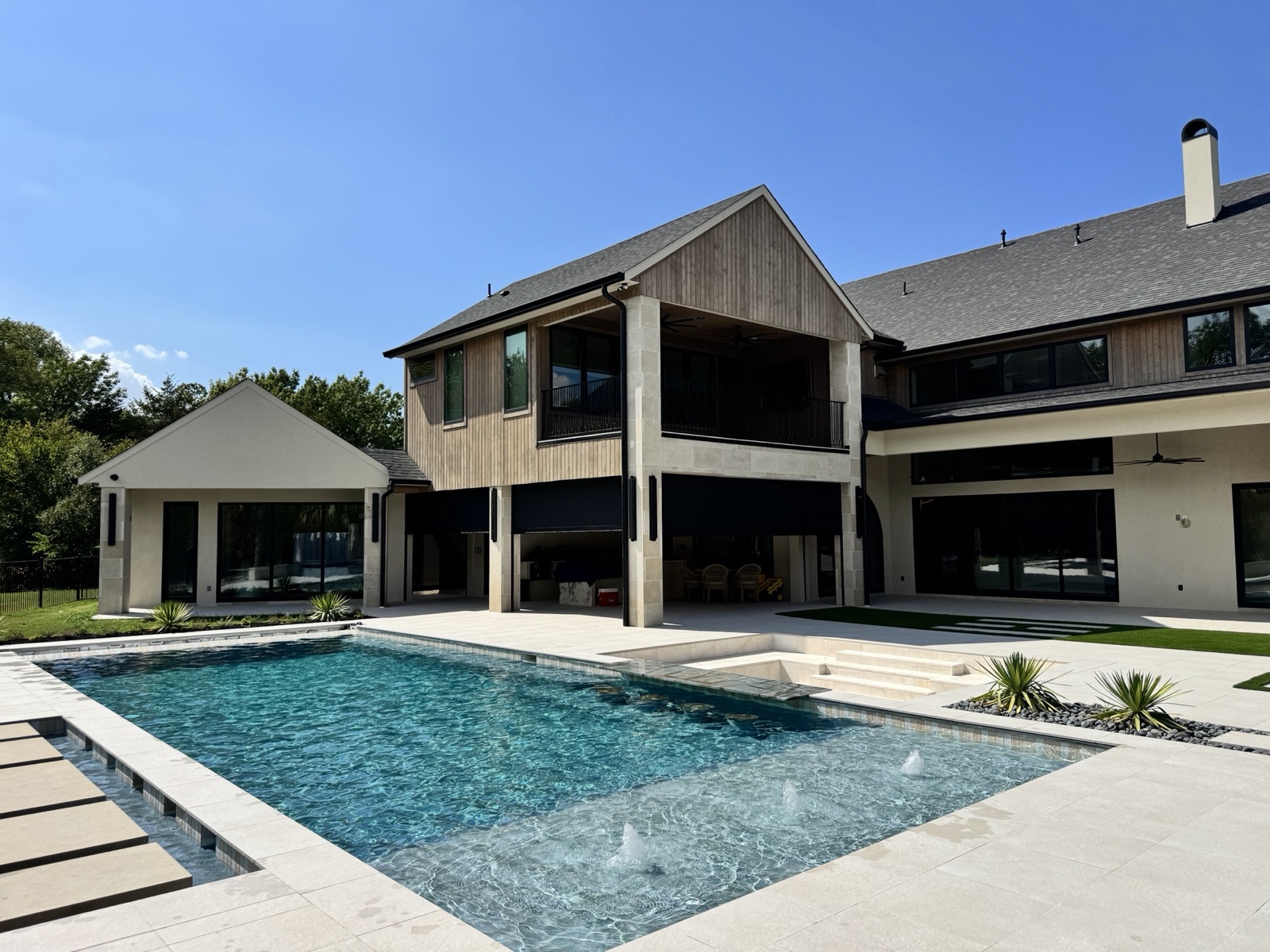 Modern two-story estate with black motorized screens across the ground-floor patio, overlooking a pool