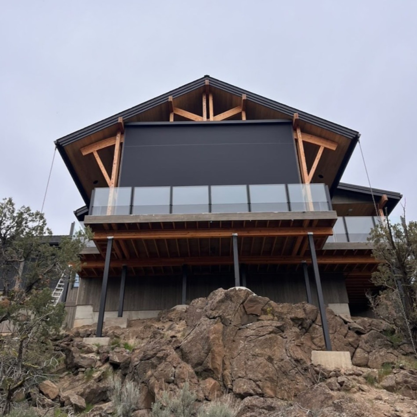 Large motorized screen filling the gable of a hillside timber-frame home above a rock outcrop