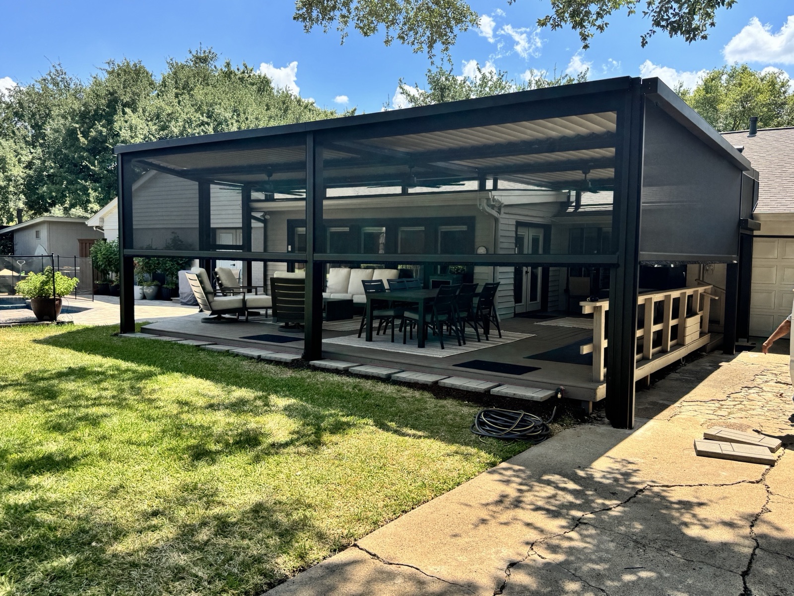 Black louvered pergola over a deck, enclosed on all sides with screens around a dining set