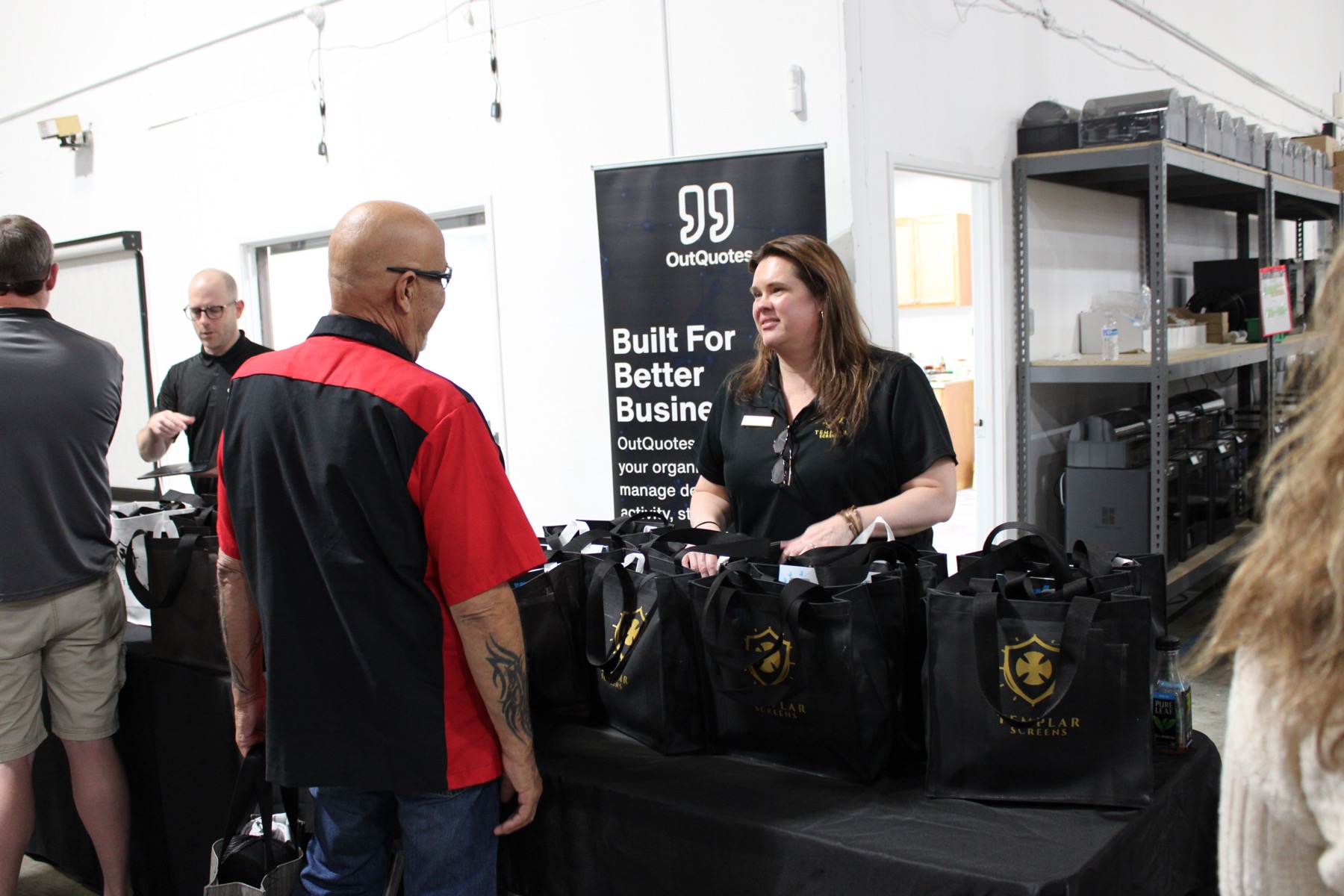 A Templar team member greeting a dealer at the OutQuotes booth, branded tote bags on the table