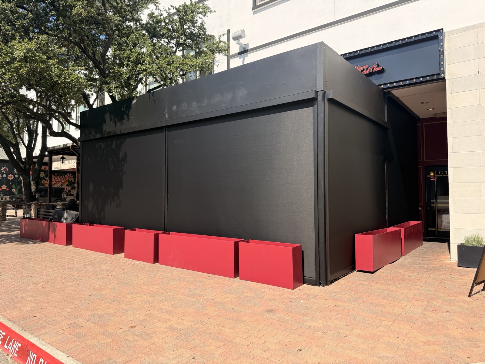 A storefront enclosed with large black motorized screens above red planters