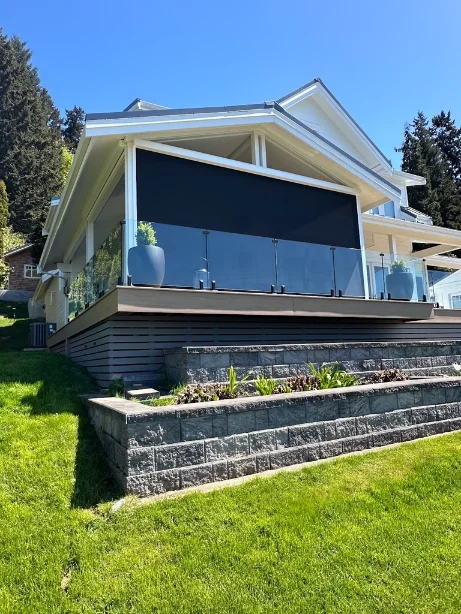 Elevated hillside deck with a dark motorized screen lowered above a glass railing