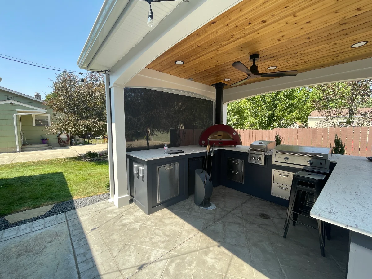 Covered outdoor kitchen with a pizza oven behind a lowered screen