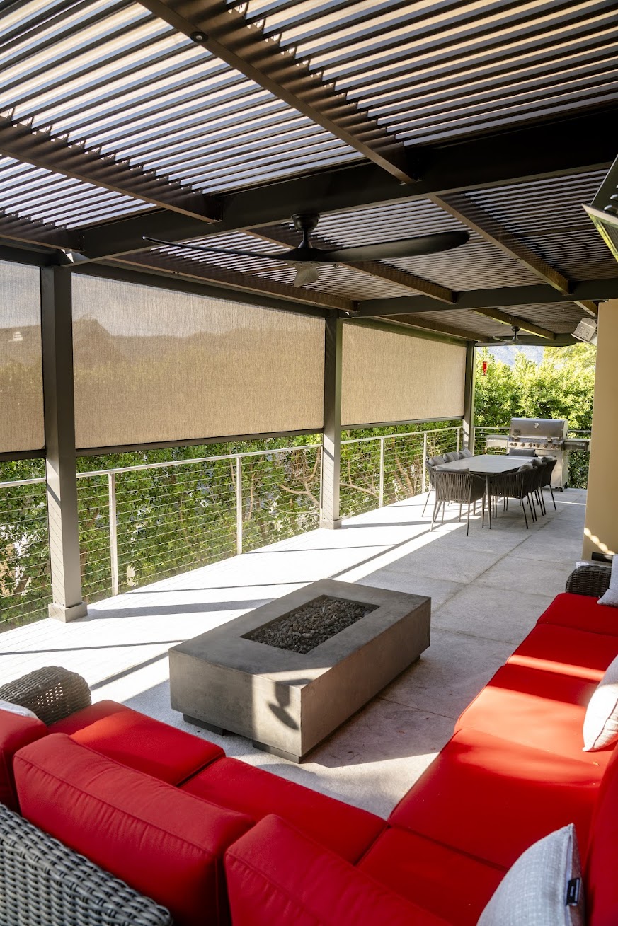 Covered deck under a pergola with tan screens lowered over a mountain view, a fire table, and red seating